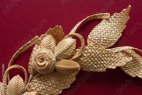 Branch with leaves and flowers is made of straw. Decoration of straw on a red background. Decor.  Straw weaving