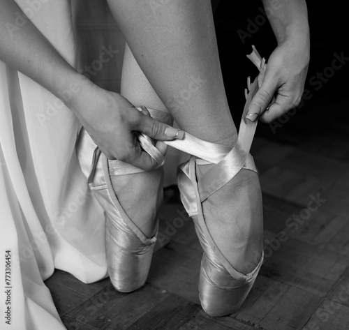 Fotografia A ballerina in a white dress and pointe shoes sits and puts on pointe shoes on a