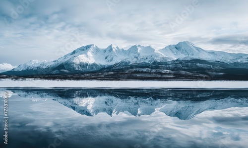 A distant view of snow-capped mountains reflected in the frozen surface of a lake © TheoTheWizard