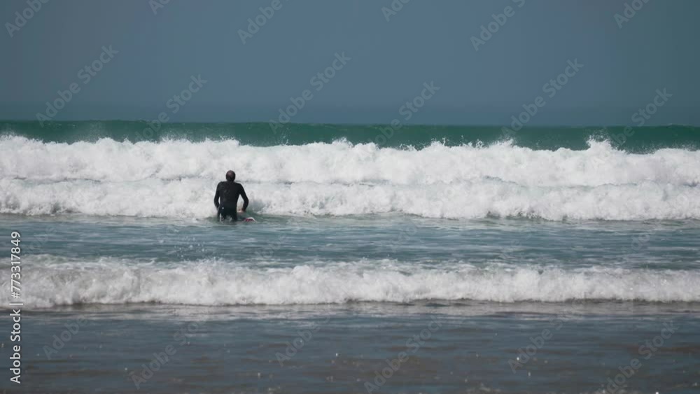 A lone surfer wearing a black wetsuit stands in the summer sea waiting for the perfect wave at Woolacombe beach in England. A lone surfer wearing a black wetsuit stands in the summer sea waiting for the perfect wave at Woolacombe beach in England.