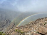 a rainbow over the mountains on top of a hill, with low clouds
