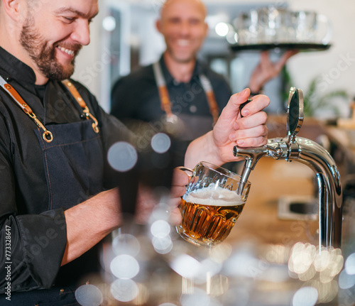 Two men friends barman and waiter with tray dressed black uniform at bar counter chatting smiling to each other. Sincere people relationships, team work, men friendship and good mood concept image.