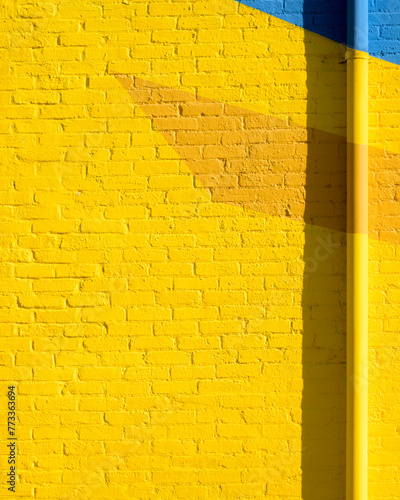 Yellow brick wall with a splash of orange and blue. There is a pipe down the right side creating a nice shadow. It would make a nice background photo