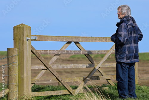 Senior standing looking over the gate at the Marsh, windy day, blue sky, he is looking in the distance at the environment with a concentrated expression, has silver hair blowing in the wind - exercise