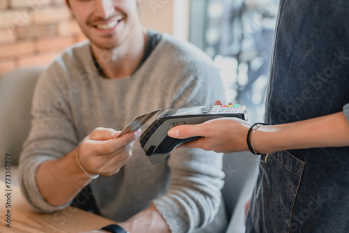 Selective focus shot of swiping machine with credit card and a man paying. Cashless payment with debit card in cafe cafeteria pub. E-banking and e-commerce mobile application