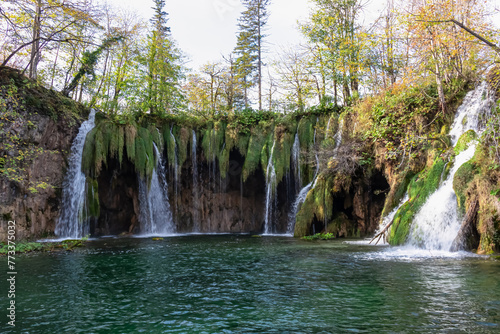 Scenic view of majestic waterfall Mali Prstavac in magical Plitvice lakes National Park, Karlovac, Croatia, Europe. Misty autumn landscape. Cascades overgrown by greenery flowing in emerald green pond