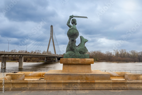A statue of a mermaid with a sword against the background of a bridge. Warsaw.