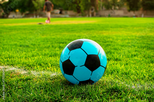 Imagen horizontal de una pelota de color azul de futbol Soccer al fondo personas practicando 