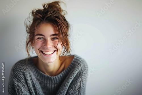 Portrait of a joyful young woman with tousled hair smiling in a cozy sweater, against a light background. photo
