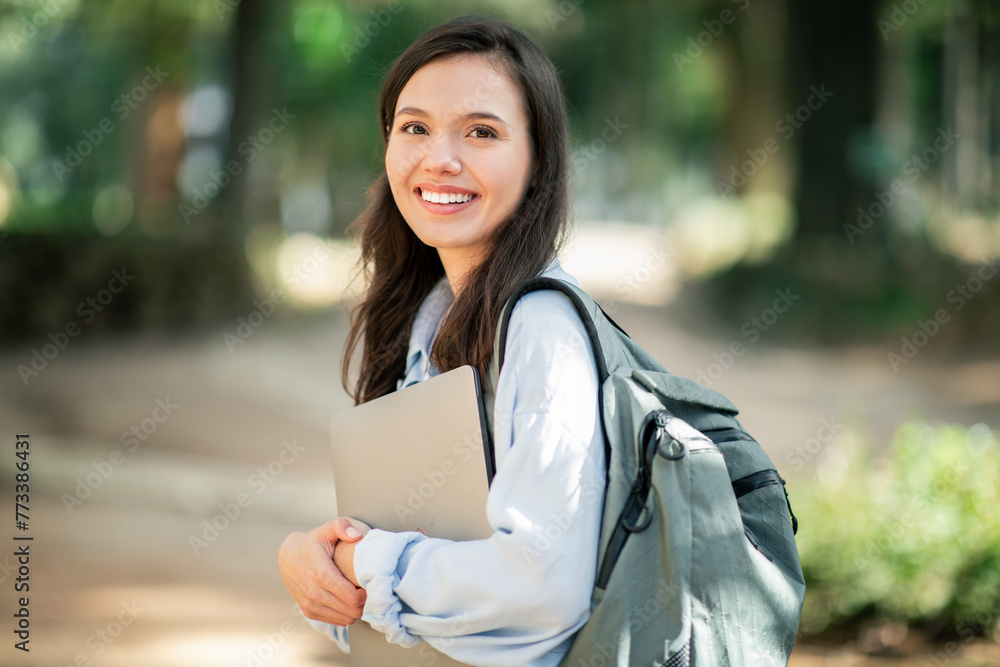 Confident young woman with a beaming smile, clutching a laptop, wearing a light blue jacket Confident young woman with a beaming smile, clutching a laptop, wearing a light blue jacket