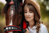 A girl in a white shirt and hat stands next to the horse.