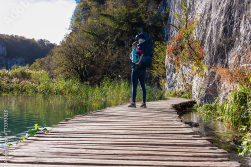 Obraz na płótnie Hiker woman with baby carrier on enchanting hiking trail on rustical wooden footpath in Plitvice lakes National Park, Karlovac, Croatia, Europe. Walking over turquoise water in idyllic paradise nature w salonie
