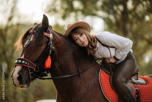 A girl in a white shirt and hat sits on a beautiful brown horse.