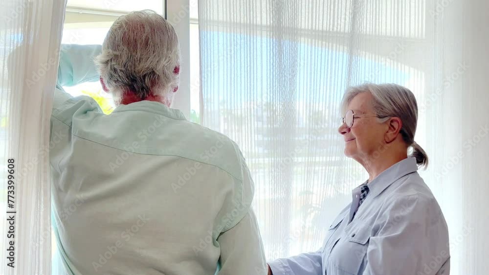 Bonding senior family couple at home looking out of the window expressing affection, elderly retired man and woman support each other Bonding senior family couple at home looking out of the window expressing affection, elderly retired man and woman support each other