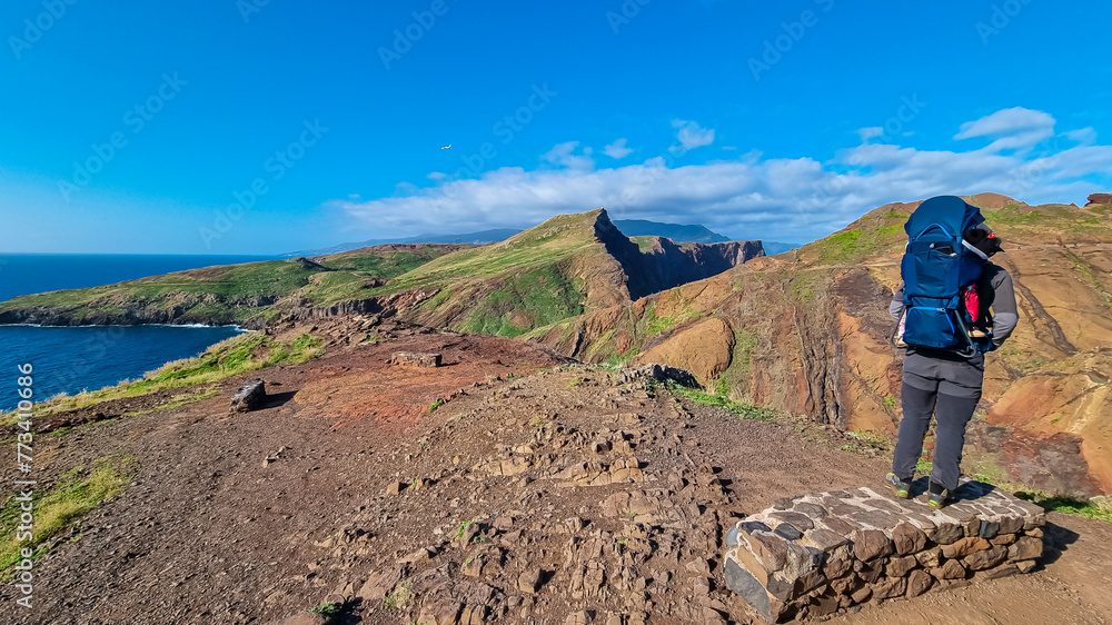 Father with baby carrier looking at majestic Atlantic Ocean coastline at Ponta de Sao Lourenco peninsula, Canical, Madeira island, Portugal, Europe. Coastal hiking trail along rocky rugged cliffs