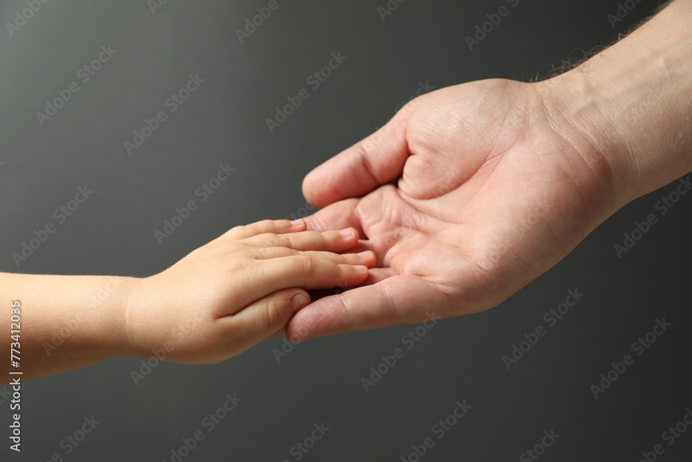 Father and child holding hands on dark grey background, closeup Father and child holding hands on dark grey background, closeup