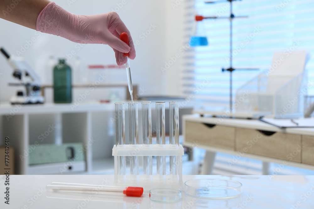 Laboratory analysis. Woman dripping liquid into test tubes at white table indoors, closeup Laboratory analysis. Woman dripping liquid into test tubes at white table indoors, closeup