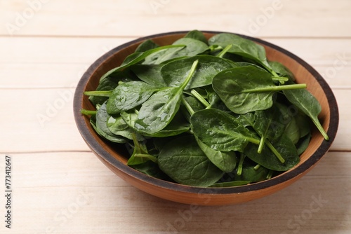 Fresh spinach leaves in bowl on light wooden table, closeup