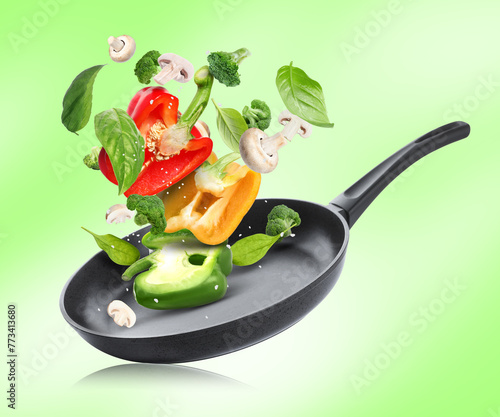 Frying pan with fresh ingredients in air on green background