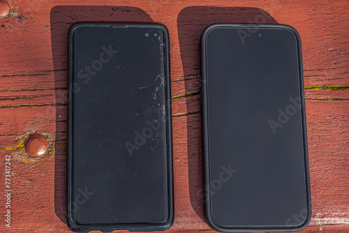 Two smartphones on a wooden bench - one old and cracked, and the other new and working