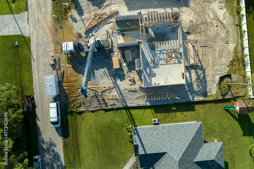 Professional builders and crane truck working on roof construction of unfinished suburban home with wooden frame structure in Florida rural area. Concept of housing development in America