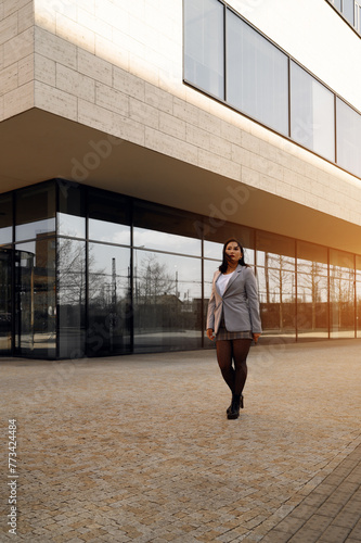 Woman in a grey suit strides in front of a modern building.