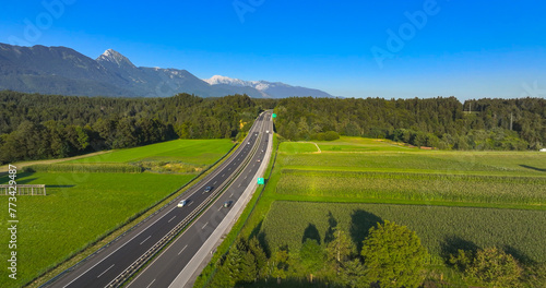 AERIAL: A drone video of a scenic green landscape, fields and a lively highway.