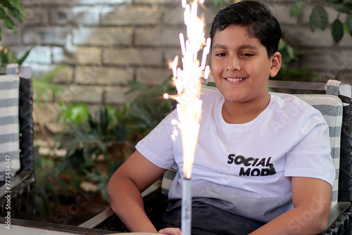 Niño latinoamericano feliz festejando su cumpleaños con una vela de chispas photo