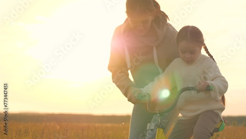 Woman teaching girl to ride bike, silhouettes at sunrise in field. Emotional support, participation, presence and encouragement from mother in learning process to help child overcome fear of failure.