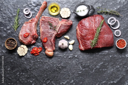 Fresh raw beef cuts and different spices on grey textured table, flat lay. Space for text