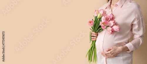 Young pregnant woman with bouquet of beautiful flowers on beige background with space for text photo