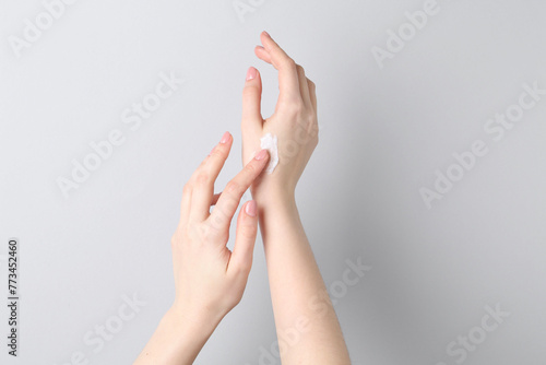 Woman applying cream on her hand against grey background  closeup
