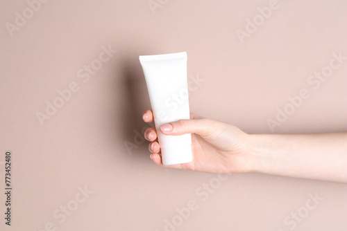 Woman with tube of cream on beige background, closeup