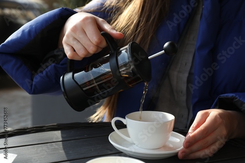 Woman pouring tea into cup at black wooden table in outdoor cafe, closeup