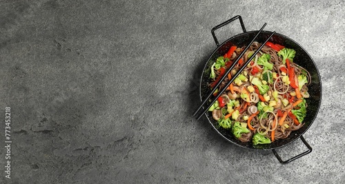 Stir fried noodles with mushrooms and vegetables in wok on grey table, top view. Space for text