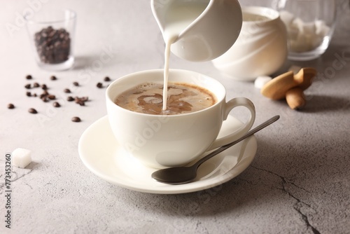 Fototapeta Naklejka Na Ścianę i Meble -  Pouring milk into cup with coffee on light grey textured table, closeup