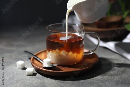 Pouring milk into cup of tea on grey table, closeup