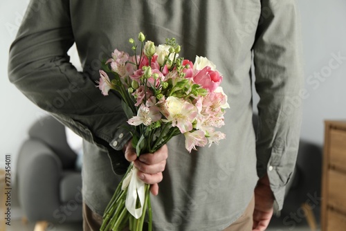 Fotografie Man hiding bouquet of flowers for his beloved woman indoors, closeup