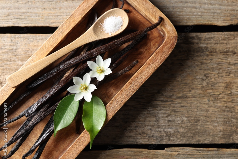 Fototapeta premium Vanilla pods, flowers, leaves and spoon with sugar on wooden table, top view