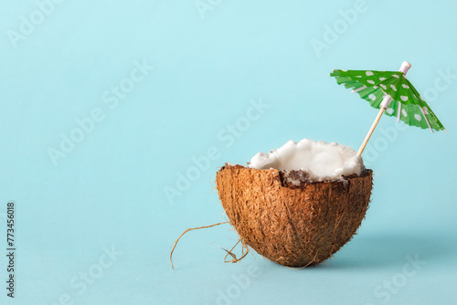 Half of a coconut cocktail with a sun umbrella on a blue background with copy space. Creative concept summer beach holiday