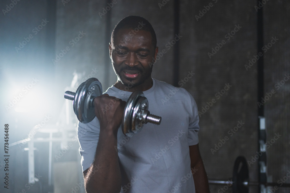 Fitness workout in gym. African American man bodybuilder picking up dumbbells in gym. Workout weight training biceps muscles with dumbbell in fitness club. Man doing sports exercise. Healthy lifestyle Fitness workout in gym. African American man bodybuilder picking up dumbbells in gym. Workout weight training biceps muscles with dumbbell in fitness club. Man doing sports exercise. Healthy lifestyle