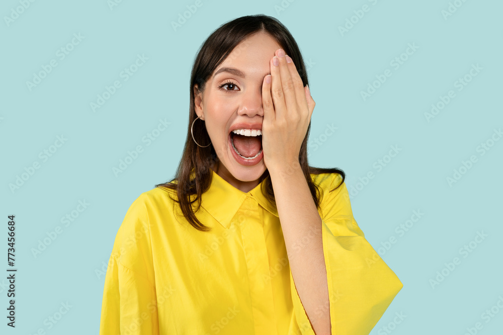 Happy surprised woman covering one eye with palm at blue studio background Happy surprised woman covering one eye with palm at blue studio background