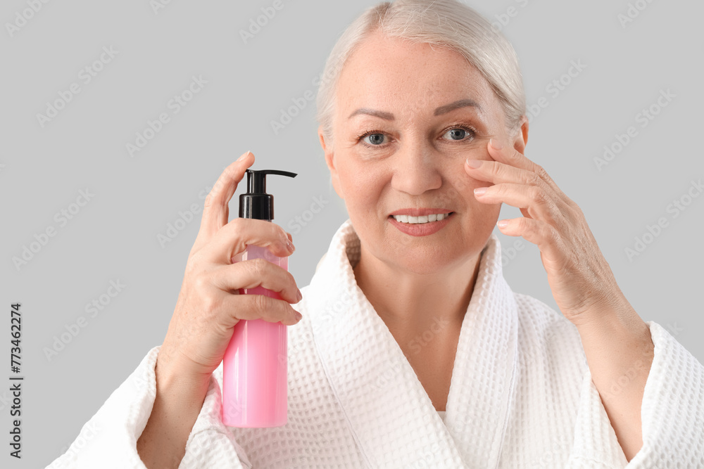 Beautiful mature woman with bottle of skincare product on light background, closeup Beautiful mature woman with bottle of skincare product on light background, closeup