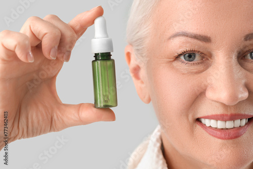 Beautiful mature woman with facial serum on light background, closeup