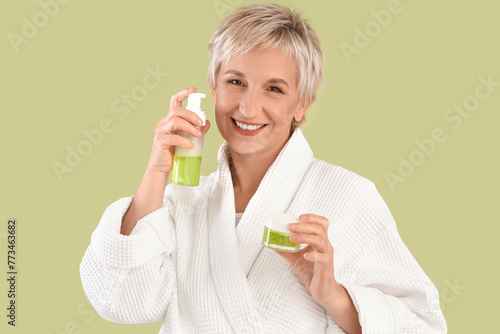 Mature woman with skincare products on green background, closeup