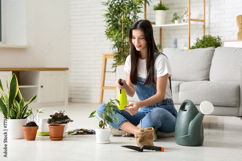 Beautiful young happy female gardener spraying water onto houseplants at home Beautiful young happy female gardener spraying water onto houseplants at home