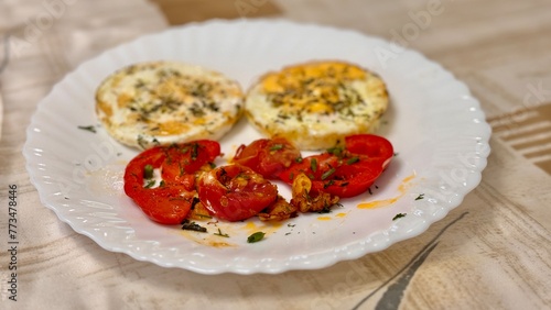 Round fried eggs with tomatoes on a white plate on a tablecloth. Close-up