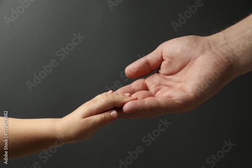 Father and child holding hands on dark grey background, closeup