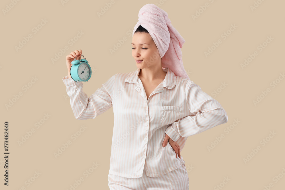 Young woman in towel with alarm clock after shower on beige background Young woman in towel with alarm clock after shower on beige background