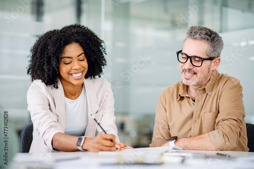 A Brazilian businesswoman in a beige blazer shares ideas with a male colleague, capturing the essence of a friendly and supportive work atmosphere where collaboration and mutual respect are valued